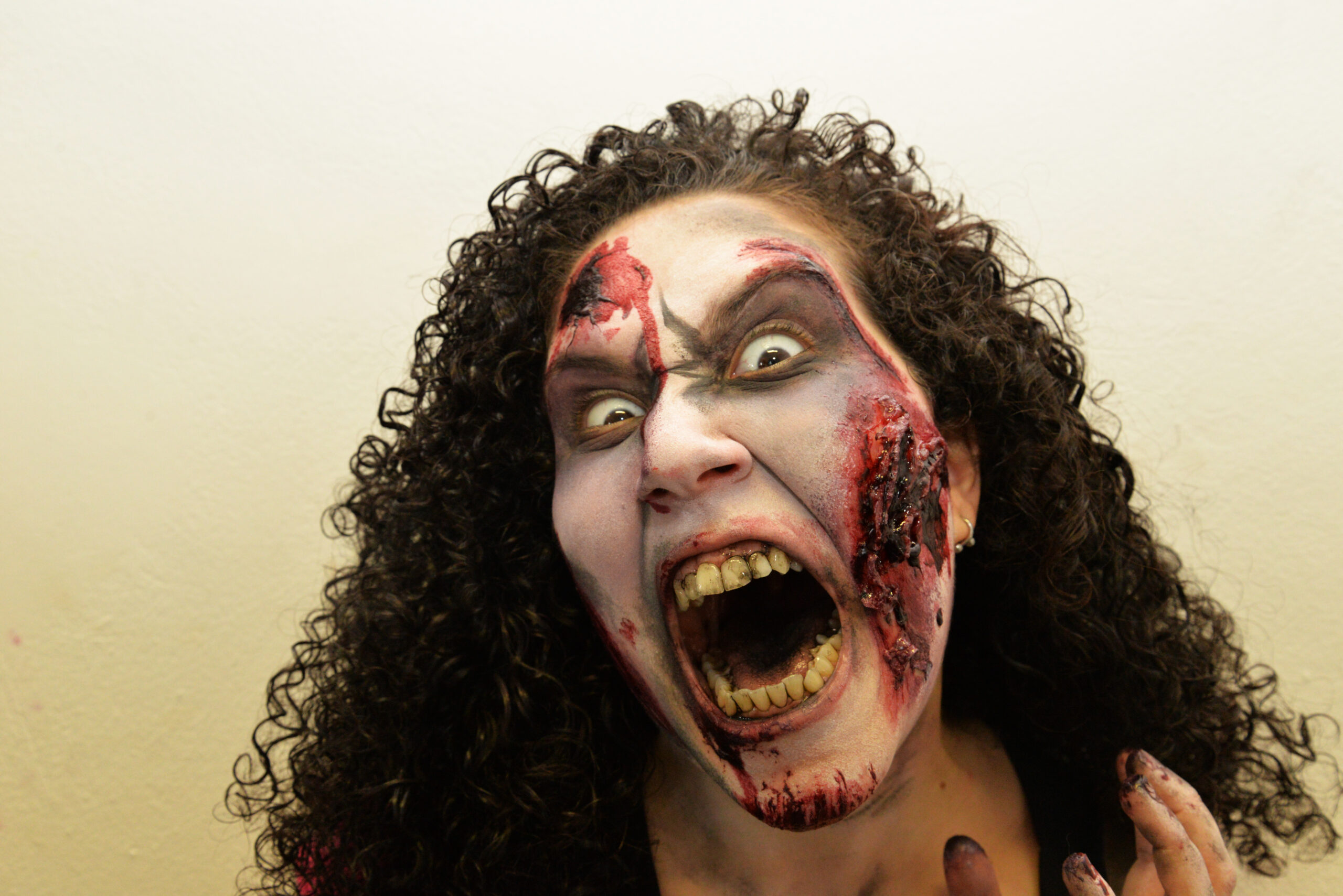 Ragazza con capelli ricci scuri, bocca spalancata e trucco horror con effetti speciali sul volto.